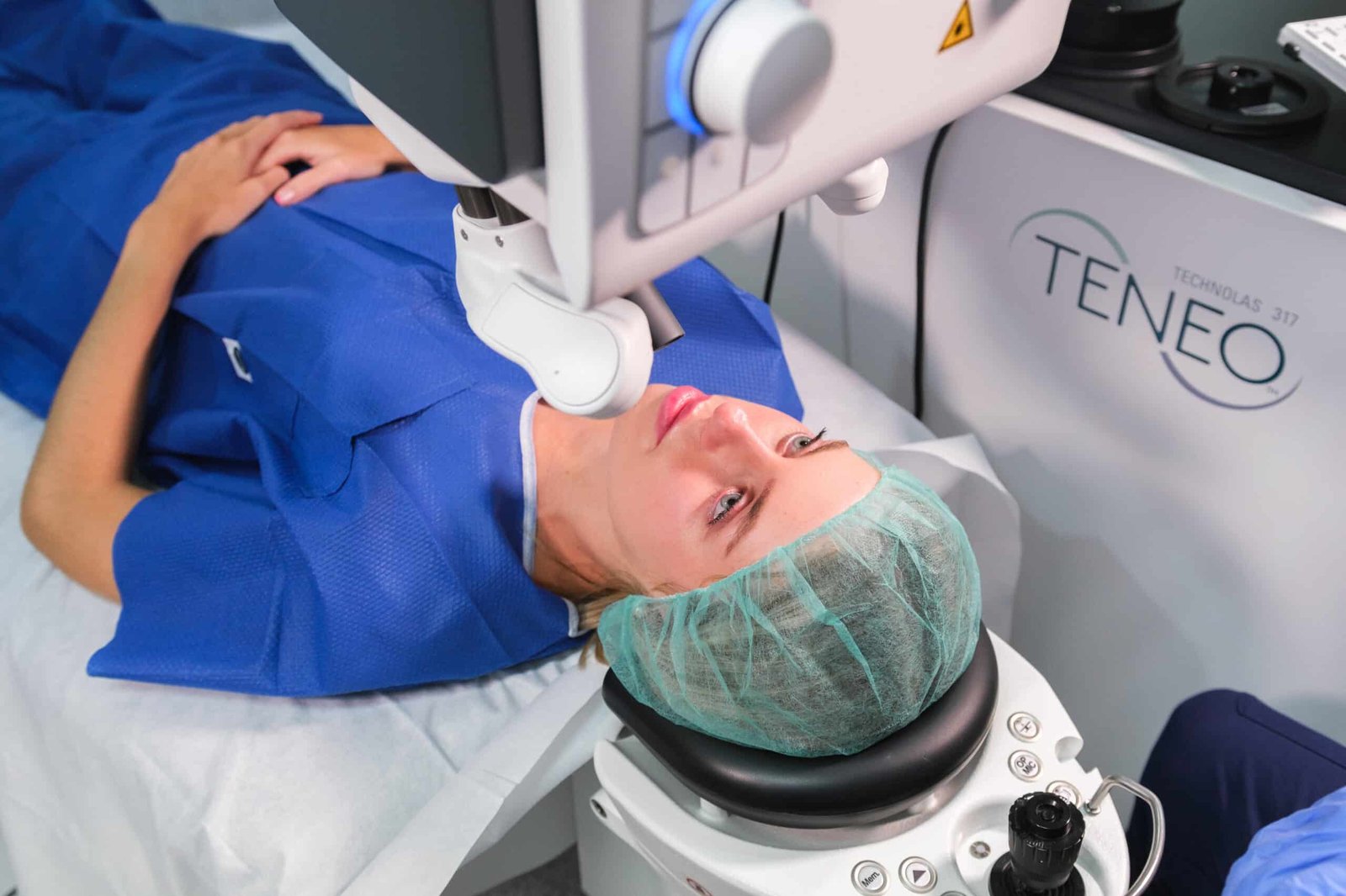 Mujer recibiendo tratamiento ocular con láser en una clínica, usando un gorro quirúrgico y una bata azul, mientras un equipo médico realiza el procedimiento.