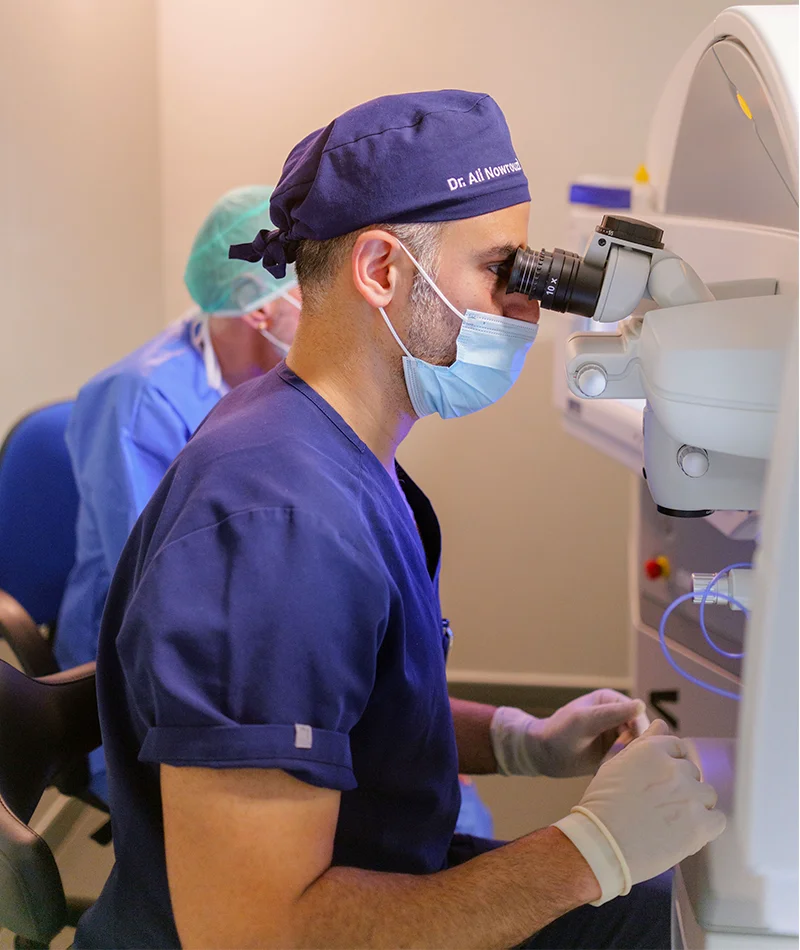 Physician using a microscope in a clinical setting, focusing on ophthalmic procedures, wearing protective equipment and gloves.